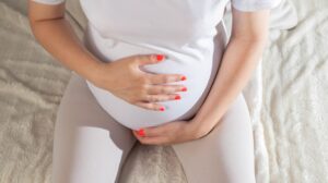 Schwangere Frau hält sich im Sitzen den Bauch.